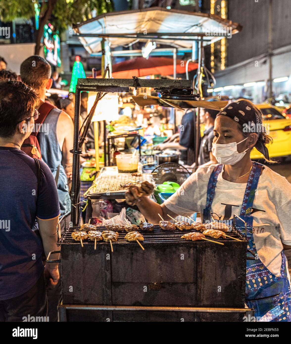 A cook prepares grilled meat skewers in a food stall at Patong Night Market in Bangkok, Thailand. Stock Photo