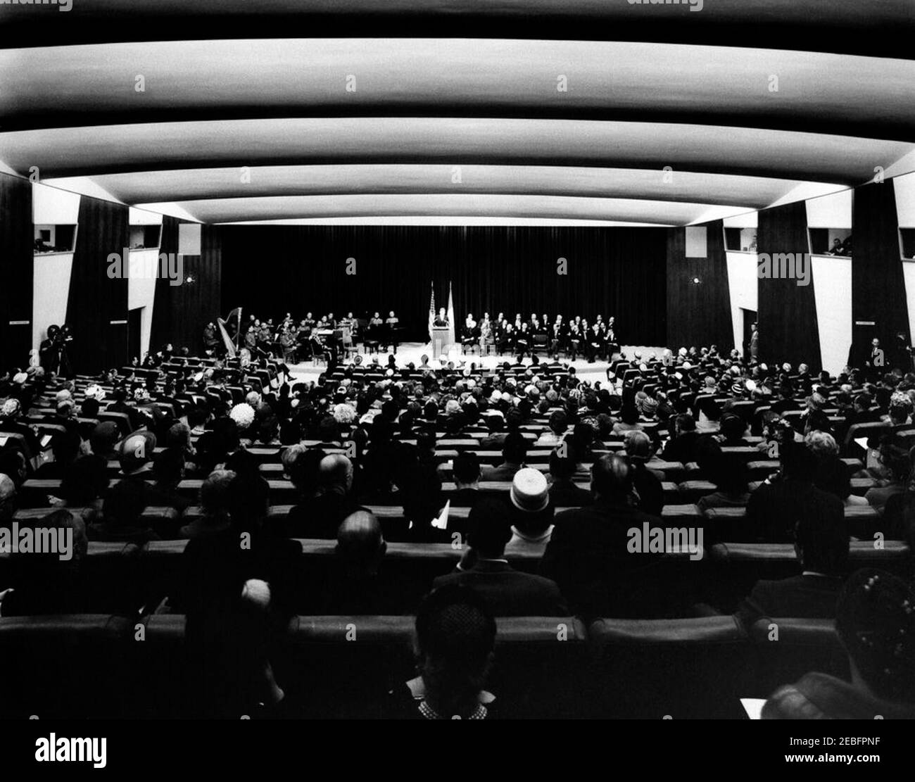 Ceremony celebrating the Unification of Italy, 10:31AM. Ceremony celebrating the Unification of Italy. Wide shot, from the back of the auditorium; President John F. Kennedy speaks from the lectern; attendees listen while seated in the audience and onstage; musicians and members of the United States Marine Band sit onstage at left. State Department Auditorium, Washington, D.C. Stock Photo