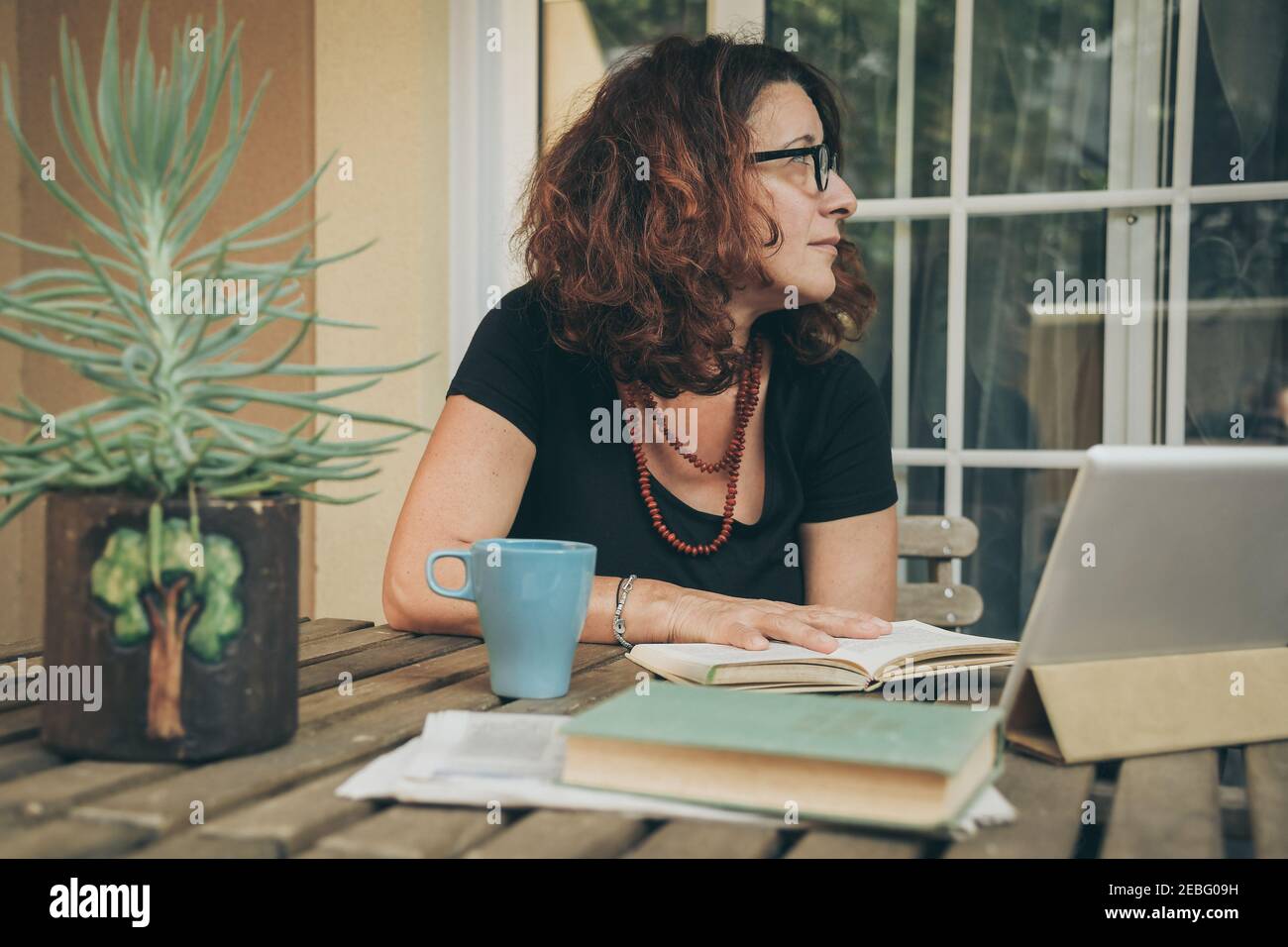 Middle aged female studying at home with books, newspaper and digital