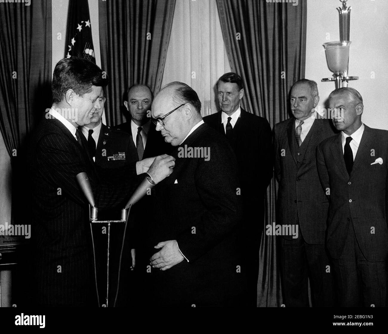 Presentation of the Medal of Freedom to Paul-Henri Spaak, Secretary General of NATO (North Atlantic Treaty Organization), 11:15AM. President John F. Kennedy presents the Medal of Freedom to Secretary General of the North Atlantic Treaty Organization (NATO) Paul-Henri Spaak, Oval Office, White House, Washington, D.C. President Kennedy pins the medal to Secretary General Spaaku2019s jacket. (L-R) Looking on: Military Aide to the President Chester V. Clifton (mostly hidden); Secretary of State Dean Rusk; United States Ambassador to NATO Warren Randolph Burgess; Former Secretary of State Dean Ach Stock Photo