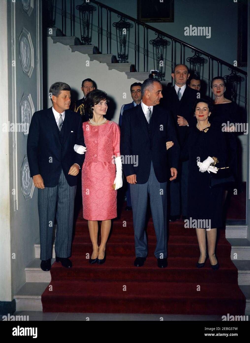 Reception for members of the Diplomatic Corps, 5:00PM. Reception for members of the Diplomatic Corps, White House, Washington, D.C. President John F. Kennedy and First Lady Jacqueline Kennedy, with Vice President Lyndon B. Johnson and Lady Bird Johnson, descend the Grand Staircase to the Entrance Hall. Behind them (L-R) are Military Aide to the President General Chester V. Clifton; Air Force Aide to the President General Godfrey McHugh; Secretary of State Dean Rusk; Naval Aide to the President Commander Tazewell Shepard, Jr. (partially hidden); Dean Rusku0027s wife Virginia Rusk. Stock Photo