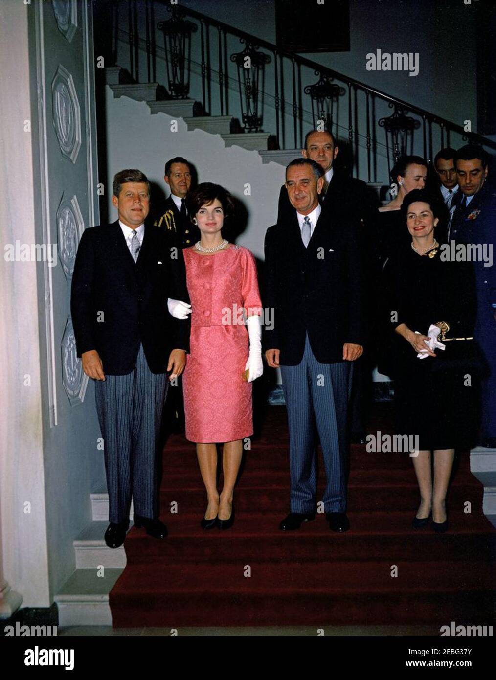 Reception for members of the Diplomatic Corps, 5:00PM. Reception for members of the Diplomatic Corps, White House, Washington, D.C. President John F. Kennedy and First Lady Jacqueline Kennedy, with Vice President Lyndon B. Johnson and Lady Bird Johnson, descend the Grand Staircase to the Entrance Hall. Behind them (L-R) are Military Aide to the President General Chester V. Clifton; Secretary of State Dean Rusk and wife Virginia Rusk; Naval Aide to the President Commander Tazewell Shepard, Jr.; Air Force Aide to the President General Godfrey McHugh. Stock Photo