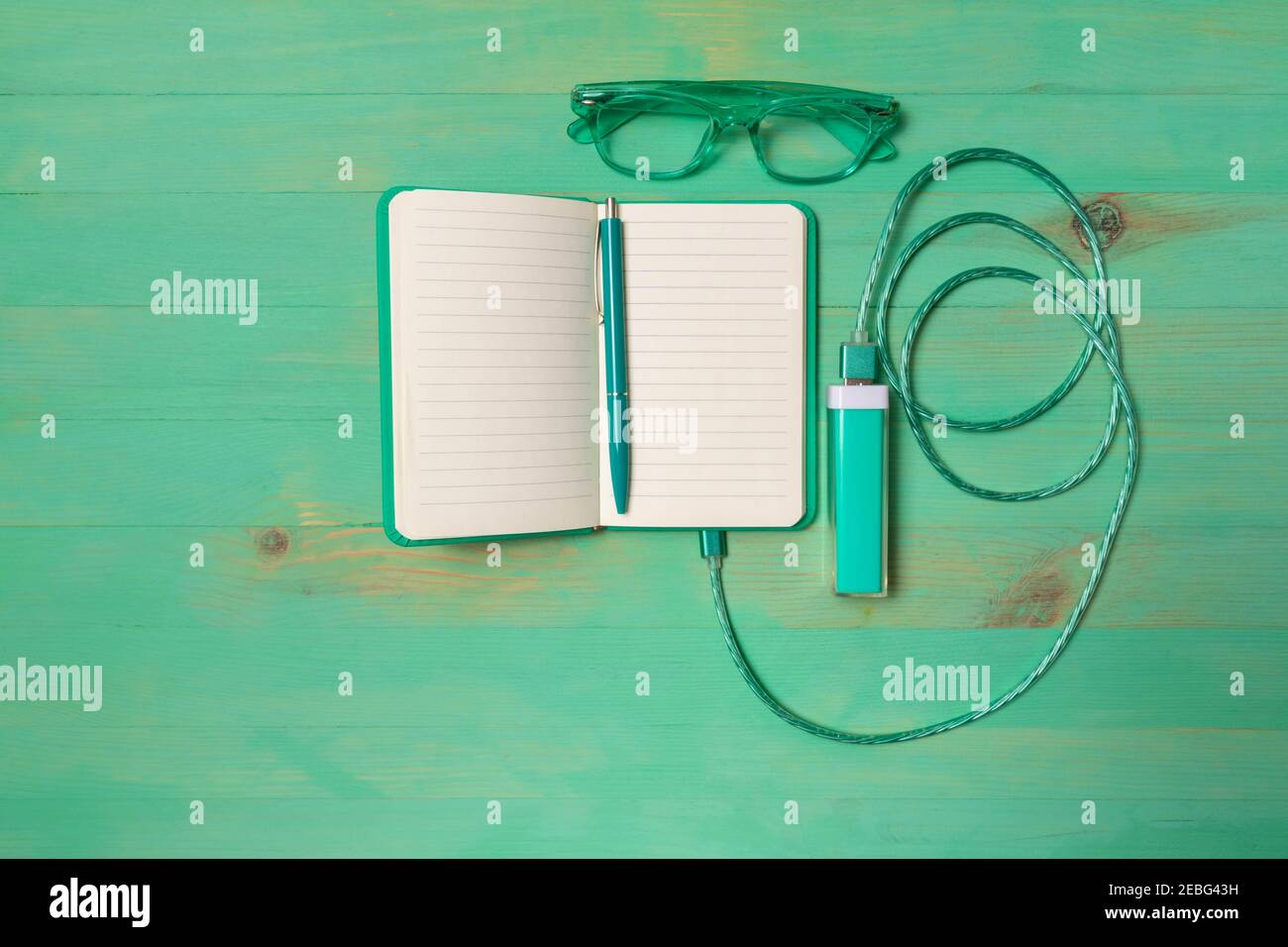 Paper notebook charging by power bank, pen and eyeglasses on wooden background. Joke imitating charging. Mockup in turquoise color. Stock Photo