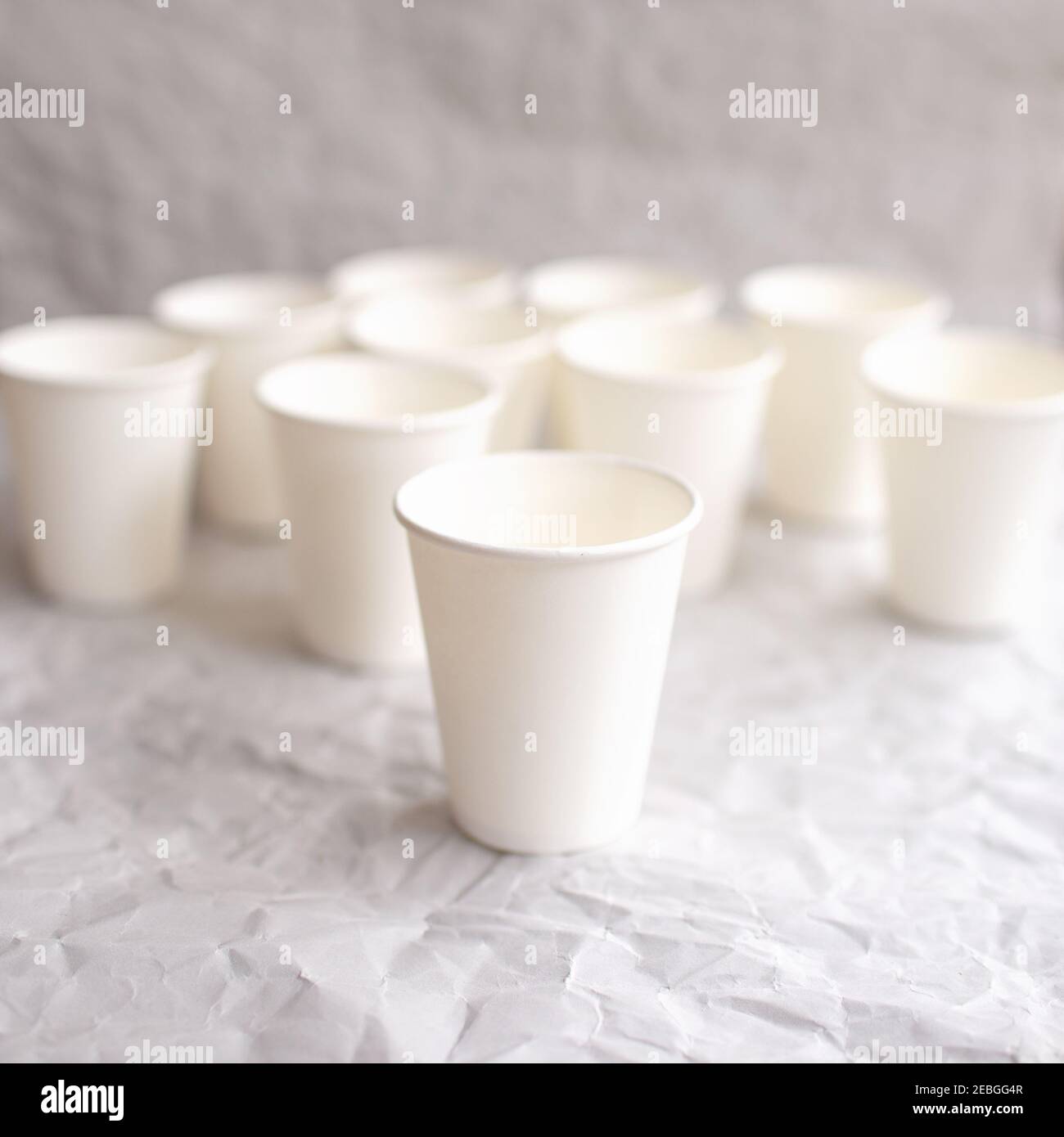 disposable cups made of white paper are laid out on gray crumpled paper in a geometric pattern Stock Photo