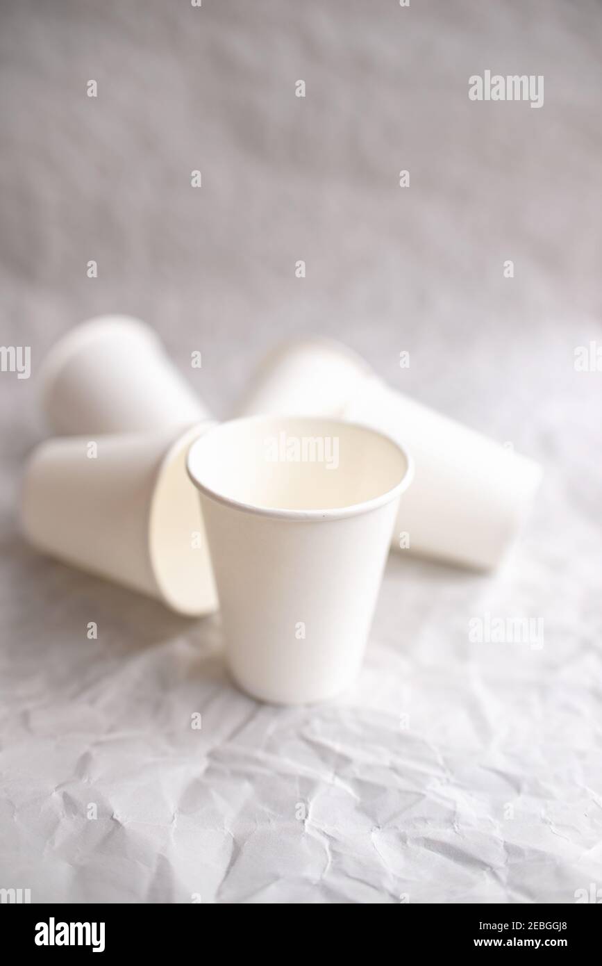 disposable cups made of white paper are laid out on gray crumpled paper in a geometric pattern Stock Photo