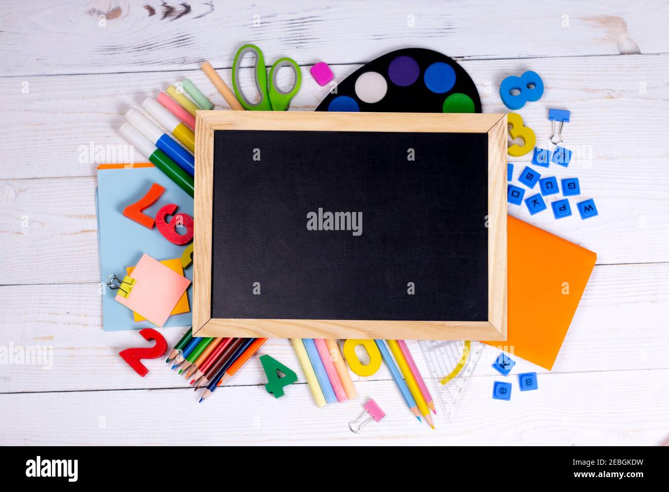 blackboard with chalk and school supplies on white wooden background ...