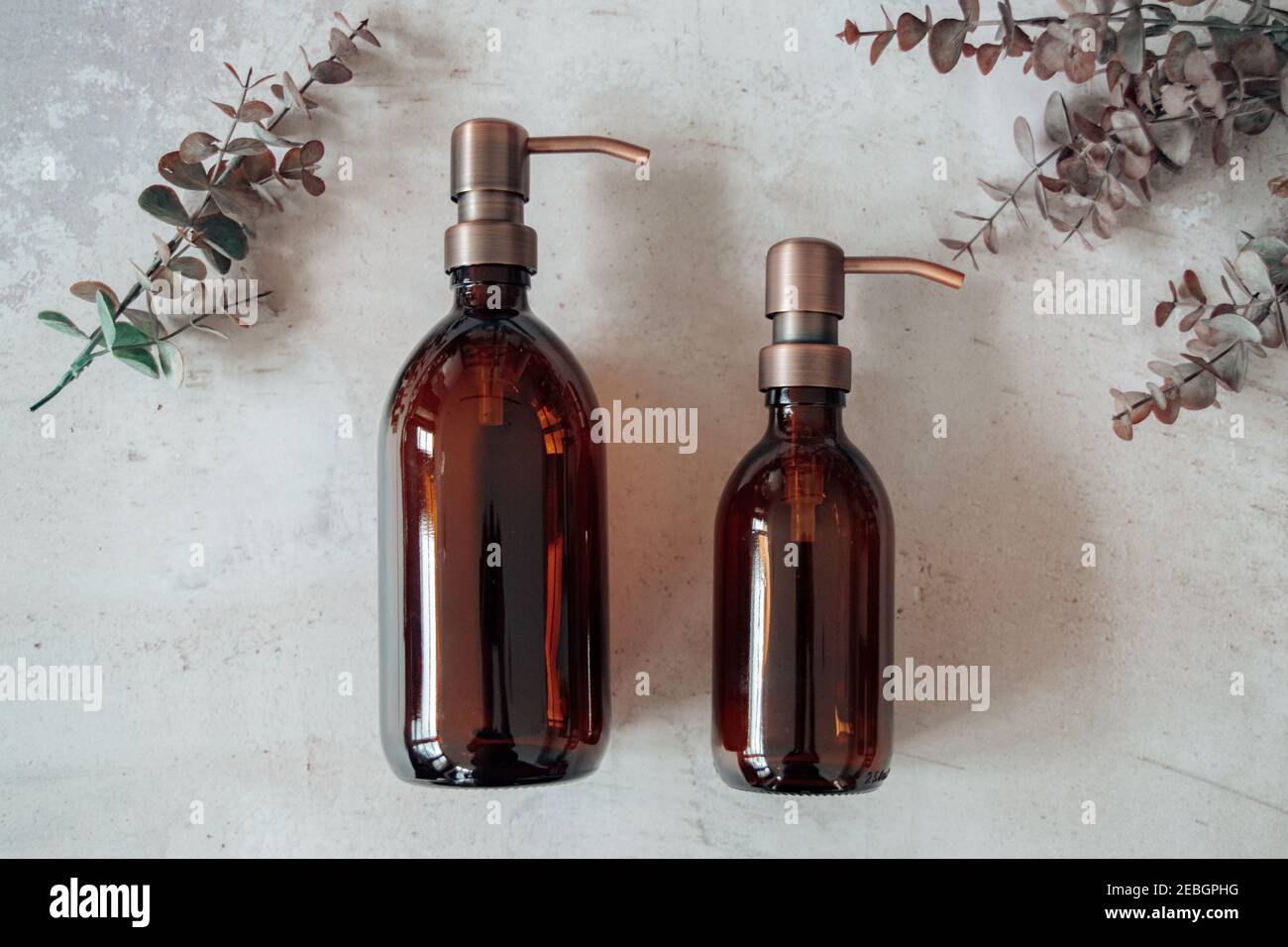 Amber glass shampoo or soap bottle dispenser with a copper steel pump against a stone background. Organic spa cosmetic product with eucalyptus. Stock Photo