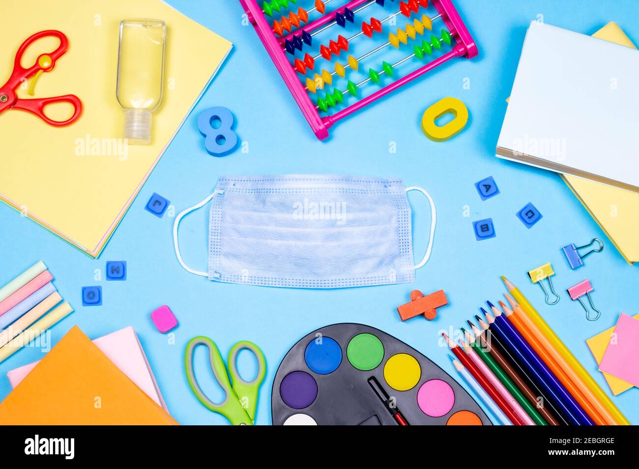Stationery accessory and medical face mask on blue background. back to School after pandemic concept. Education, office and freelancer work flat lay c Stock Photo