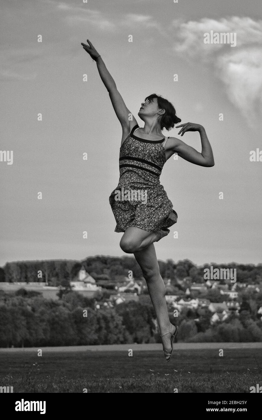 Beautiful young and elegant female dancer jumping high in the sky, in black and white Stock Photo