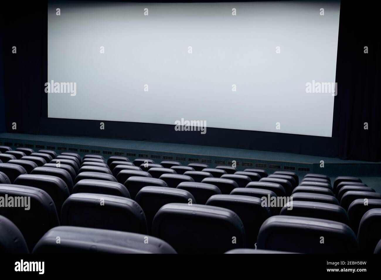 Cinema hall with white screen and black row chairs. Concept of empty