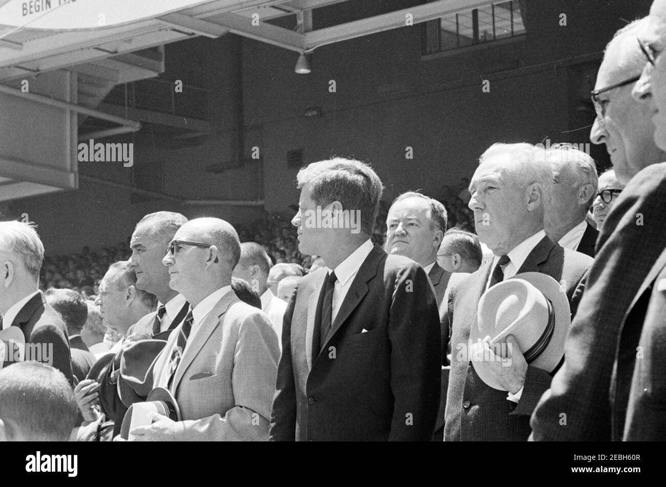 1962 All Star Baseball Game at D.C. Stadium, 12:52PM. President John F. Kennedy and others stand for the National Anthem during the 32nd Major League Baseball (MLB) All-Star Game at D.C. Stadium, Washington, D.C. Those pictured with President Kennedy include: Vice President Lyndon B. Johnson; Special Assistant to the President, Dave Powers; Senator Hubert H. Humphrey (Minnesota); Commissioner of Baseball, Ford C. Frick; Deputy Special Counsel to the President, Myer Feldman. [Scratch in upper right corner of image is original to the negative.] Stock Photo