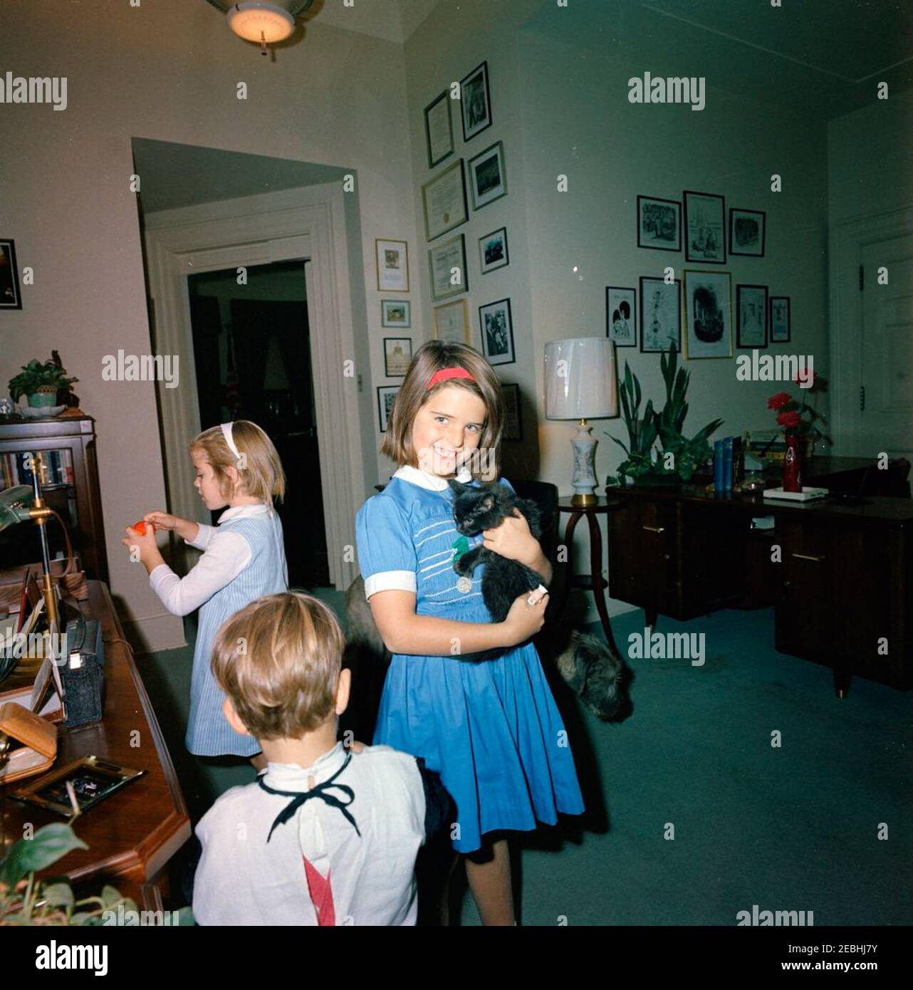 President Kennedy with Caroline Kennedy (CBK) u0026 John F. Kennedy, Jr. (JFK, Jr.), in Halloween costumes. Caroline Kennedy, John F. Kennedy, Jr., and Maria Shriver (holding a cat) play in the office of President John F. Kennedyu2019s Personal Secretary, Evelyn Lincoln. Kennedy family dog, Wolf, stands in background. White House, Washington, D.C. Stock Photo