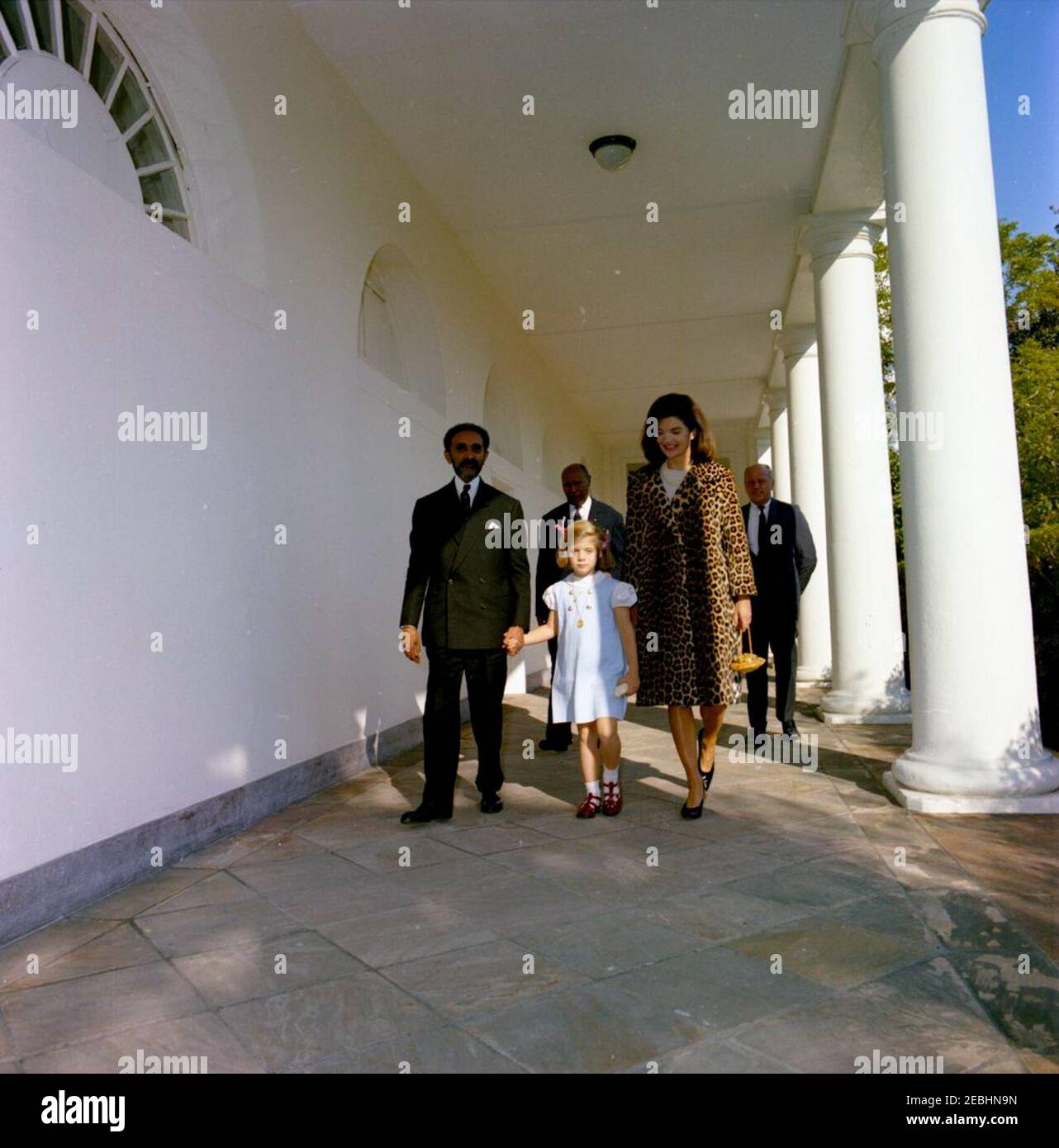 Meeting with Haile Selassie I, Emperor of Ethiopia, 4:33PM. First Lady Jacqueline Kennedy walks with Emperor of Ethiopia, Haile Selassie I, and Caroline Kennedy along the West Wing Colonnade of the White House. Walking behind are Minister of the Imperial Court of Ethiopia, Tafarra-Worq Kidane-Wold, and U.S. State Department Protocol officer, Jay Rutherfurd. Emperor Selassie presented as gifts to the Kennedy family a leopard coat and gold filigree jewelry case for Mrs. Kennedy and carved ivory figurines for Caroline and John F. Kennedy, Jr. Washington, D.C. Stock Photo