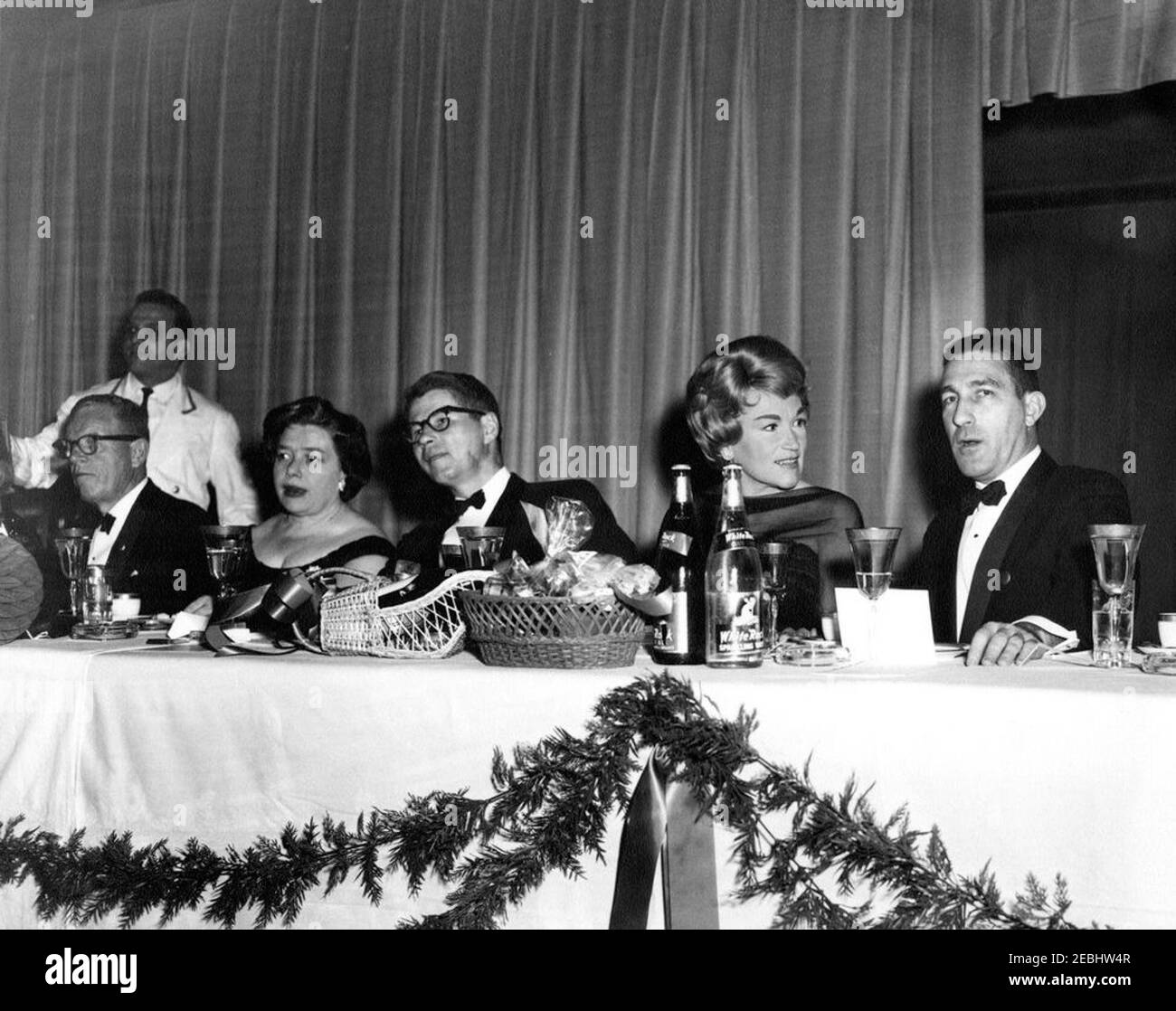 National Cultural Center Fund-raising benefit, 9:23PM. Guests attend a fundraising dinner and closed-circuit telecast of u0022An American Pageant of the Artsu0022 for the National Cultural Center. Seated (L-R): two unidentified persons; Secretary of Agriculture, Orville L. Freeman; opera singer Dorothy Kirsten; and Secretary of the Interior, Stewart L. Udall. National Guard Armory, Washington, D.C. Stock Photo