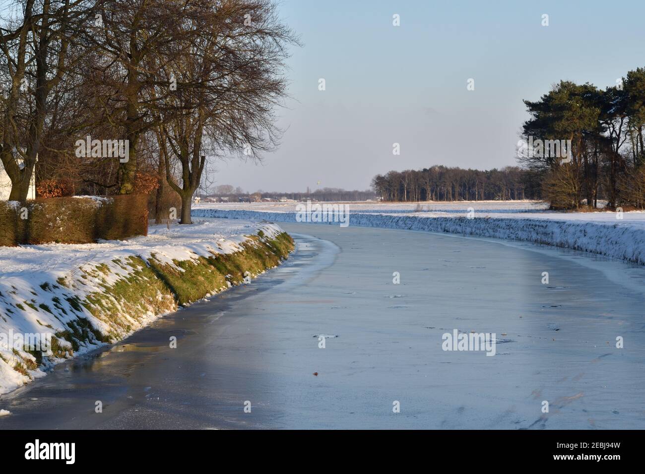 A frozen canal in the Netherlands beside snow covered fields under a blue winter sky Stock Photo