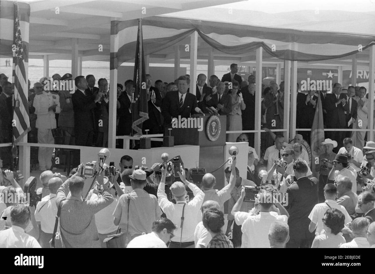 Trip to Western States: Los Banos, California (San Luis Dam), 11:40AM. President John F. Kennedy (at lectern) delivers remarks at the groundbreaking ceremony for the San Luis Dam in Los Banos, California. Those standing on speakersu0027 platform include: Secretary of the Interior, Stewart L. Udall; Senators Thomas H. Kuchel and Clair Engle (both of California); Under Secretary of the Interior, James K. Carr. White House Secret Service agents, Bob Lilley and Win Lawson, stand in front of platform; members of the press observe. Stock Photo