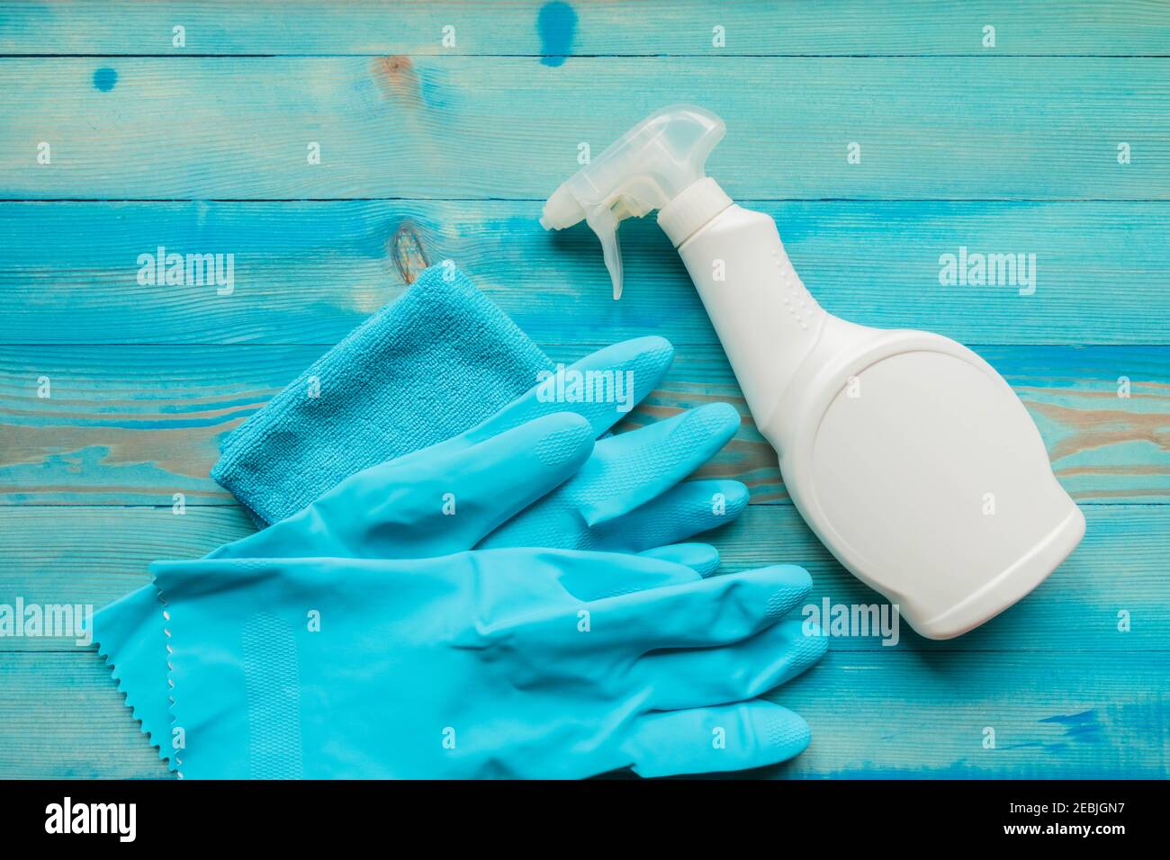 Cleaning supplies for disinfection. White spray bottle with disinfectant liquid, blue rubber gloves and microfiber cloth on blue wooden background. Hy Stock Photo