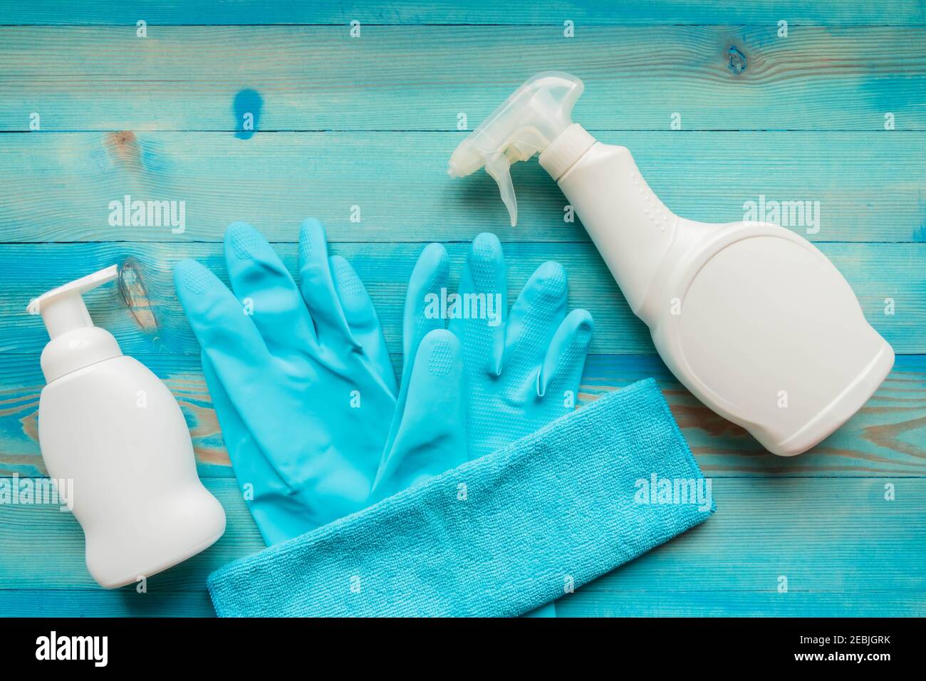 Cleaning products for disinfection. Blue rubber gloves, microfiber cloth and white spray bottles with disinfectant liquid on blue wooden background. H Stock Photo