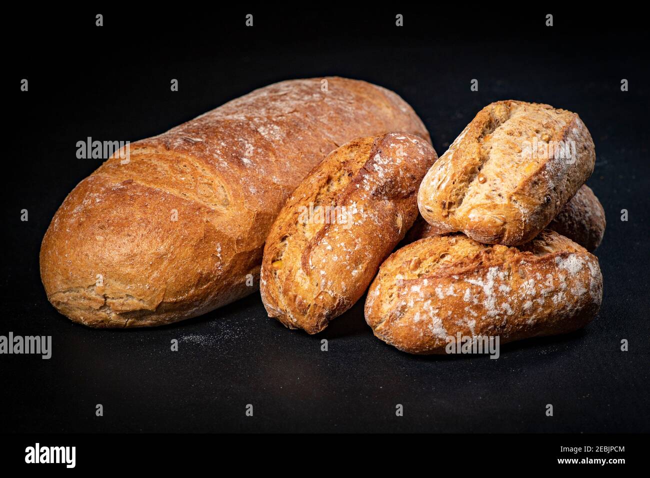 Fresh bread and rolls on a black kitchen table. Bread prepared for serving. Dark background. Stock Photo