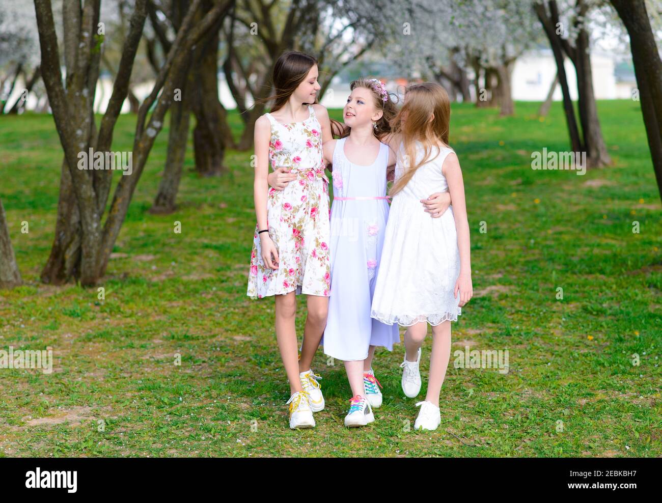 Three adorable girls in dresses hold hands in a circle holding hands ...
