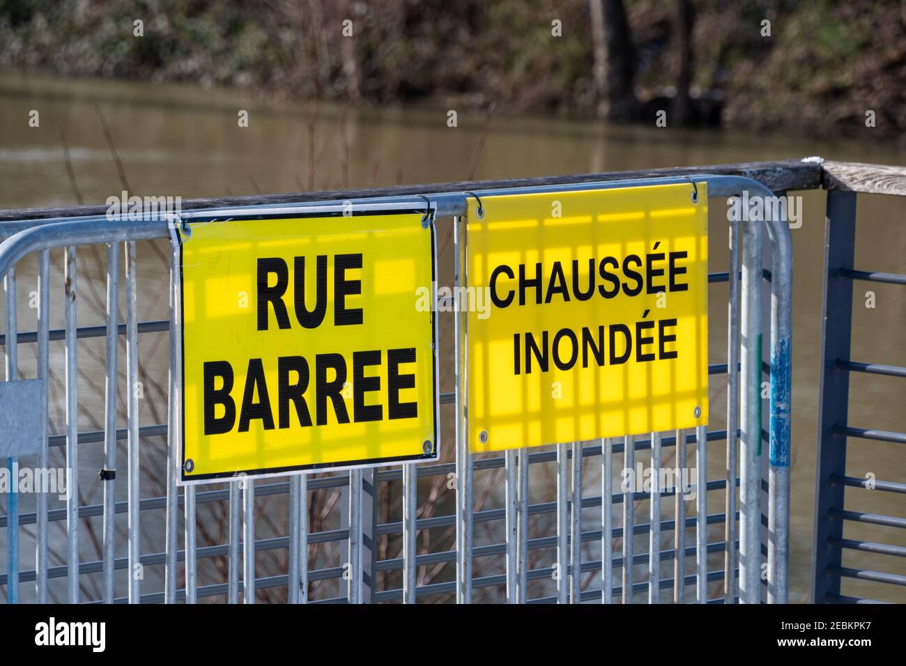 Weather - Flood warnings in France. Two yellow warning signs fixed on a metal fence and written in French: "Closed street" and "Flooded pavement" Stock Photo