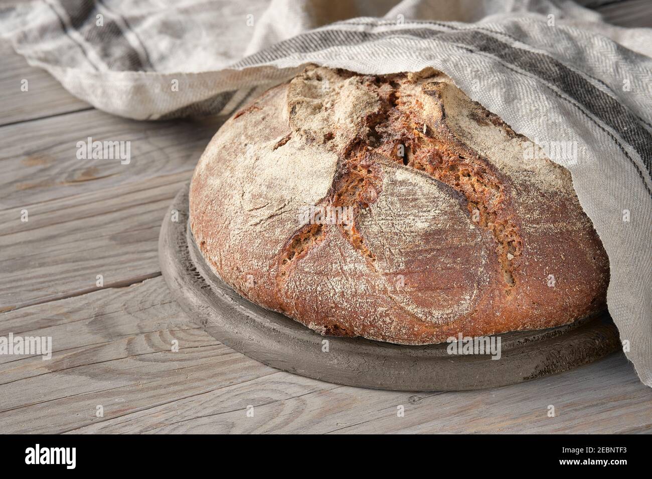 No knead handmade loaf on cutting board on wood with linen towel, spelt ears. German Bauernbrot means Farmers Bread in English. Wholemeal rye wheat Stock Photo