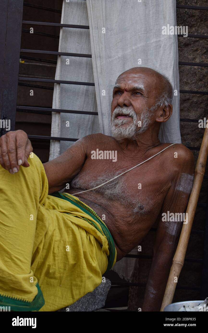 Priest portrait image in Badavilinga Temple with stick wearing yellow dhoti relaxing /Shiva Linga Hampi Stock Photo