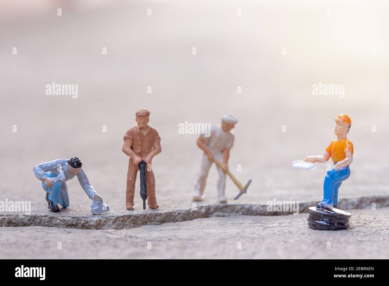 Miniature people- Figures construction worker, is working on a cracked area with blurred background and sunlight.Business and construction concept. Stock Photo