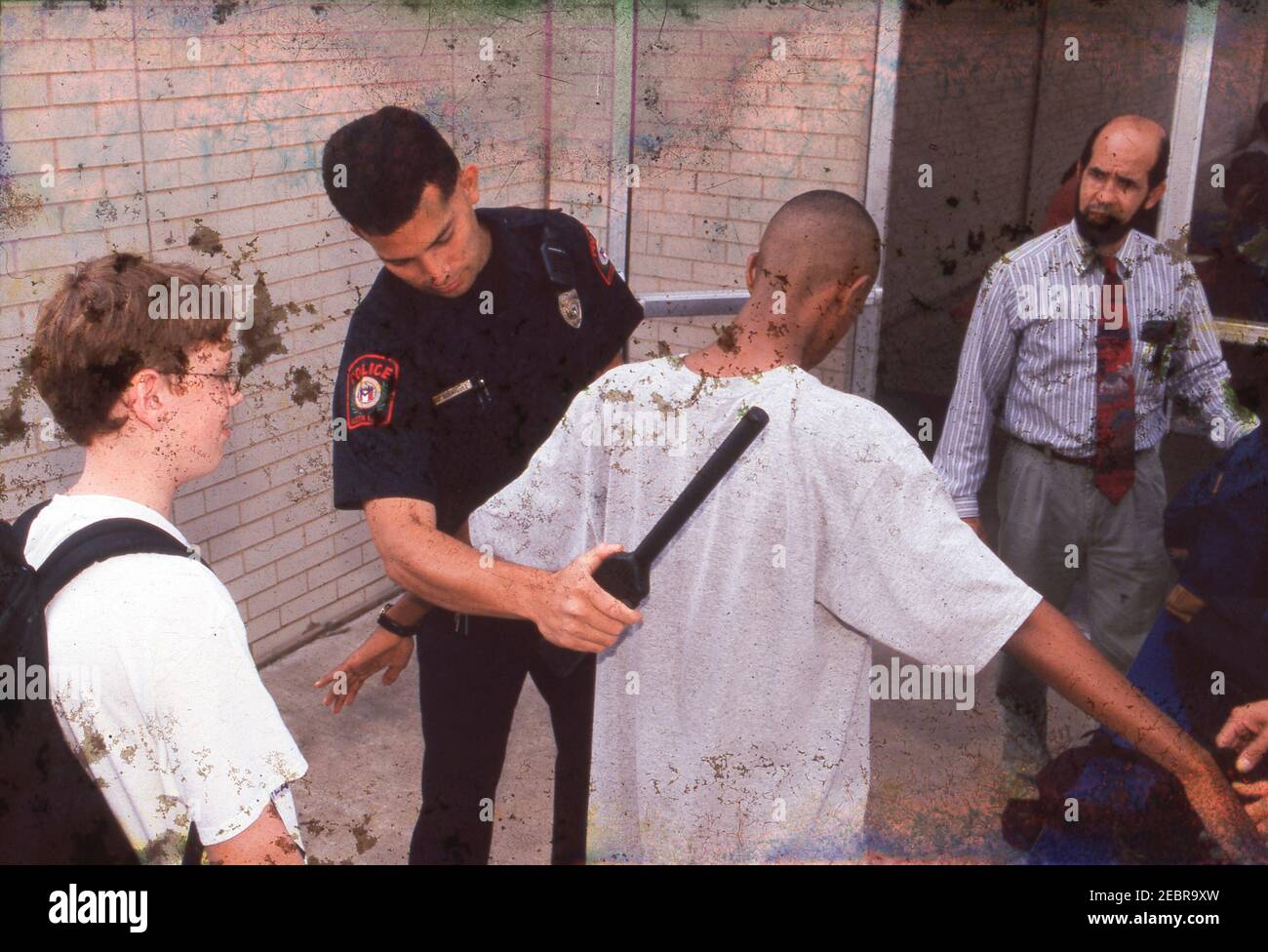 Austin Texas USA, circa 1997:  A school police officer uses a metal detector while a teacher inspects backpacks as students enter their middle school at the beginning of the school day. ©Bob Daemmrich Stock Photo