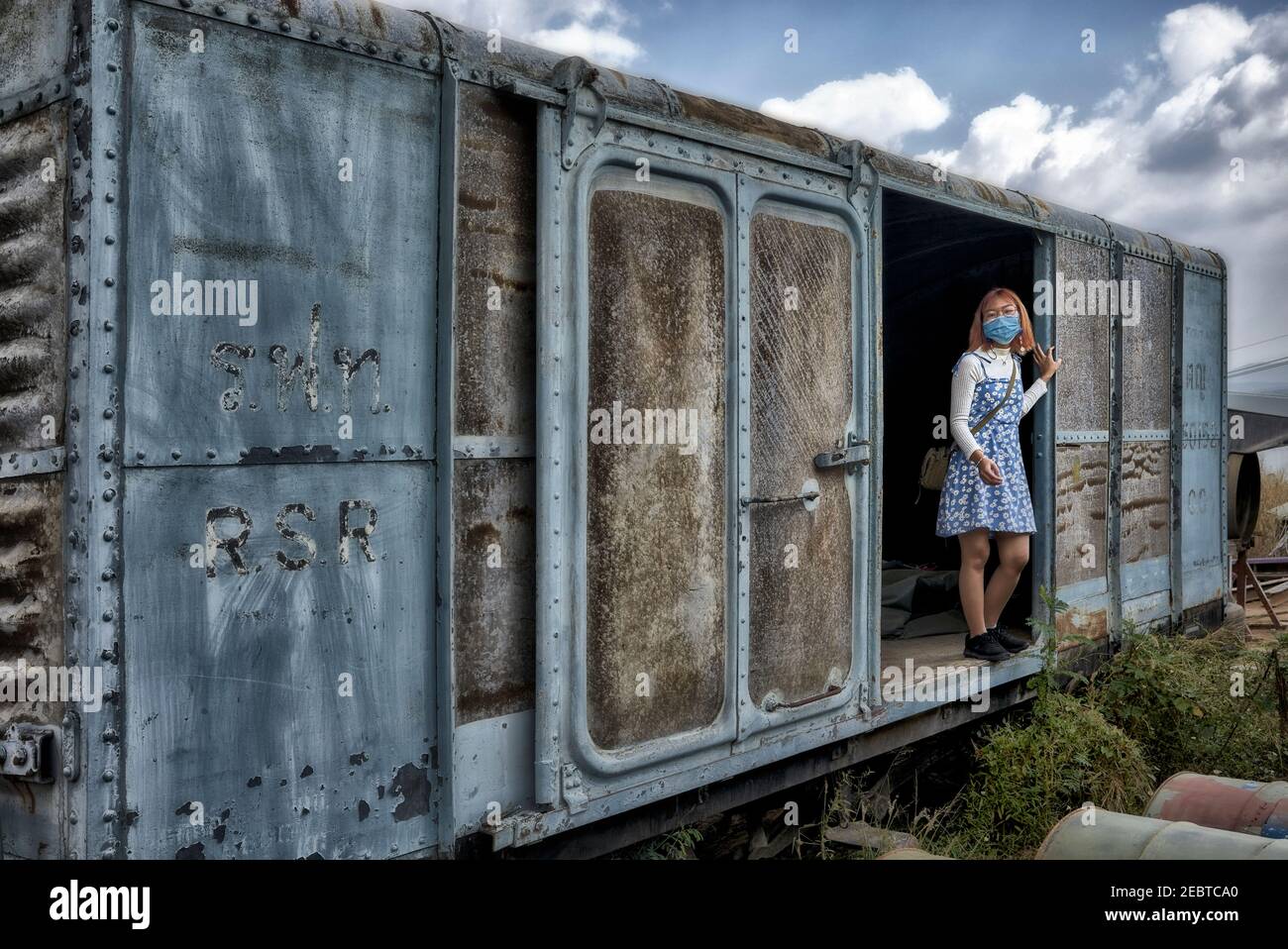 Girl in a train scrap yard posing for a photograph inside a disused rusting vintage railway goods carriage. Thailand, Southeast Asia. Freight wagon Stock Photo