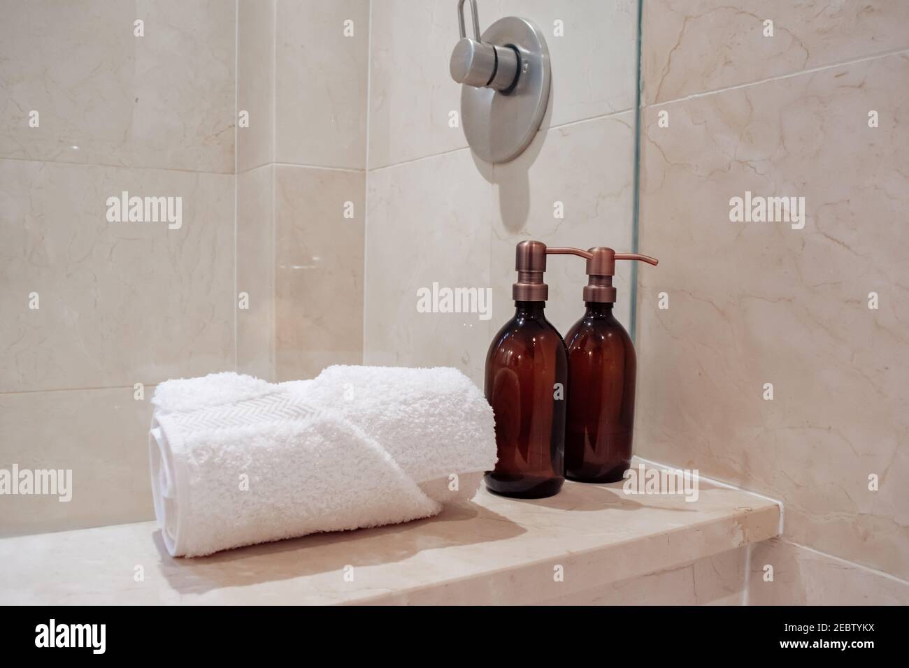 Amber glass shampoo bottles with copper steel pumps in a luxury marble hotel spa and shower. Stock Photo