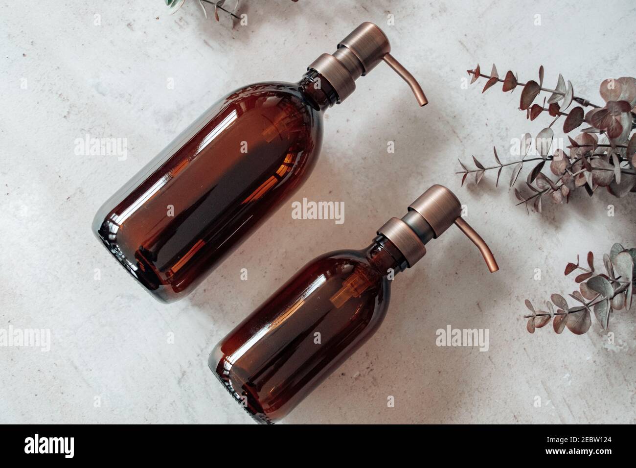 Amber glass shampoo or soap bottle dispenser with a copper steel pump against a stone background. Organic spa product with eucalyptus. Stock Photo