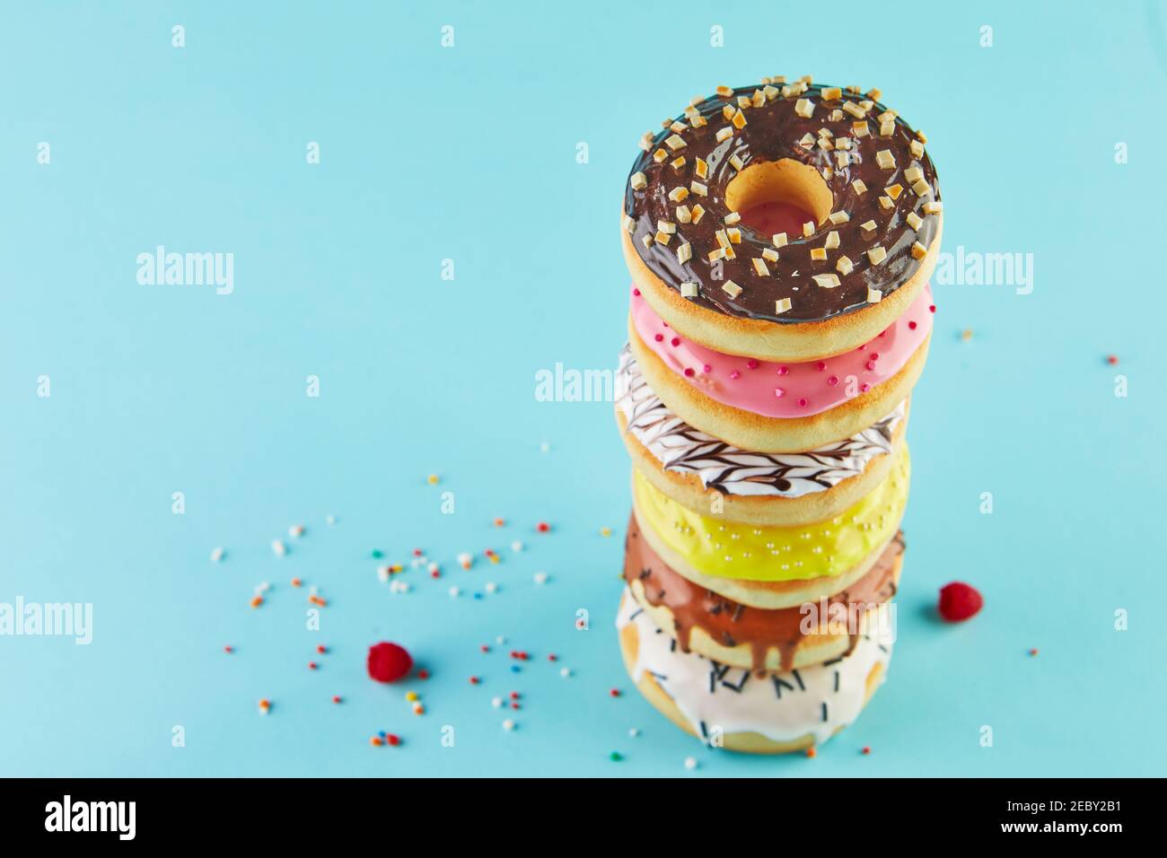Multicolored donuts with icing and sprinkling stacked in a stack on a blue background. Stock Photo