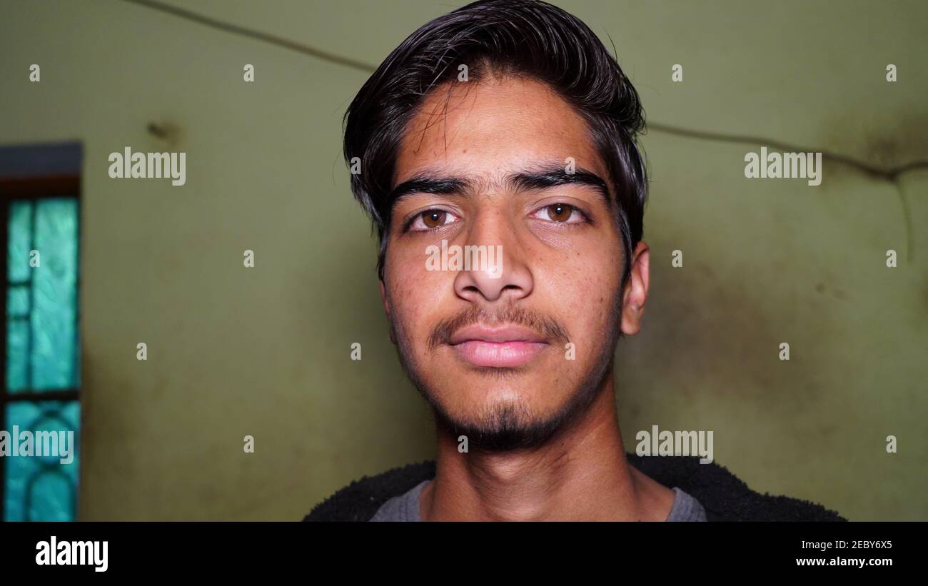 Portrait of a young Indian boy looking with peace at the camera. Isolated facial shot closeup with wall background. Stock Photo
