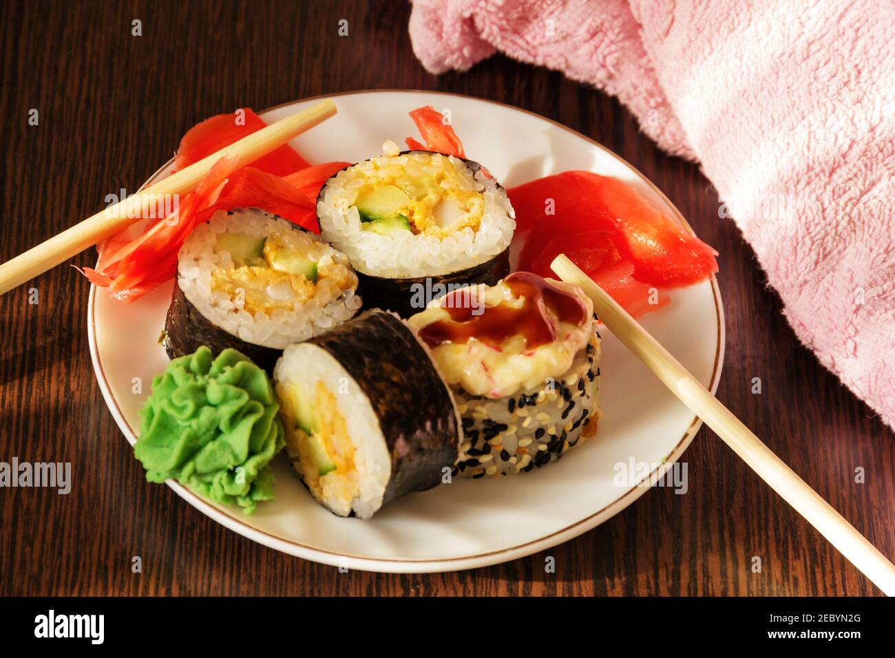 A dish of Japanese cuisine. Ready-made rolls on a white plate with wasabi sauce and pickled ginger. Stock Photo