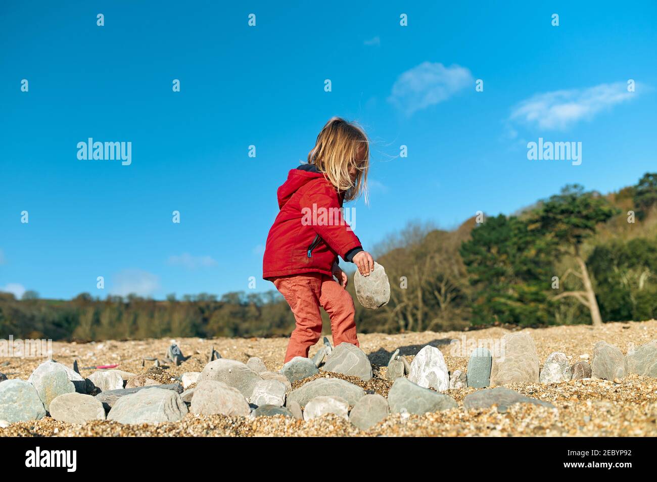 A little preschooler is playing with rocks on the beach in the winter Stock Photo
