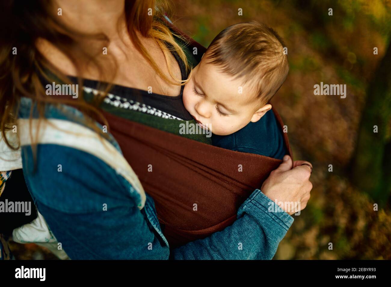 A young mother is in the woods with her baby in a sling on an autumn day Stock Photo