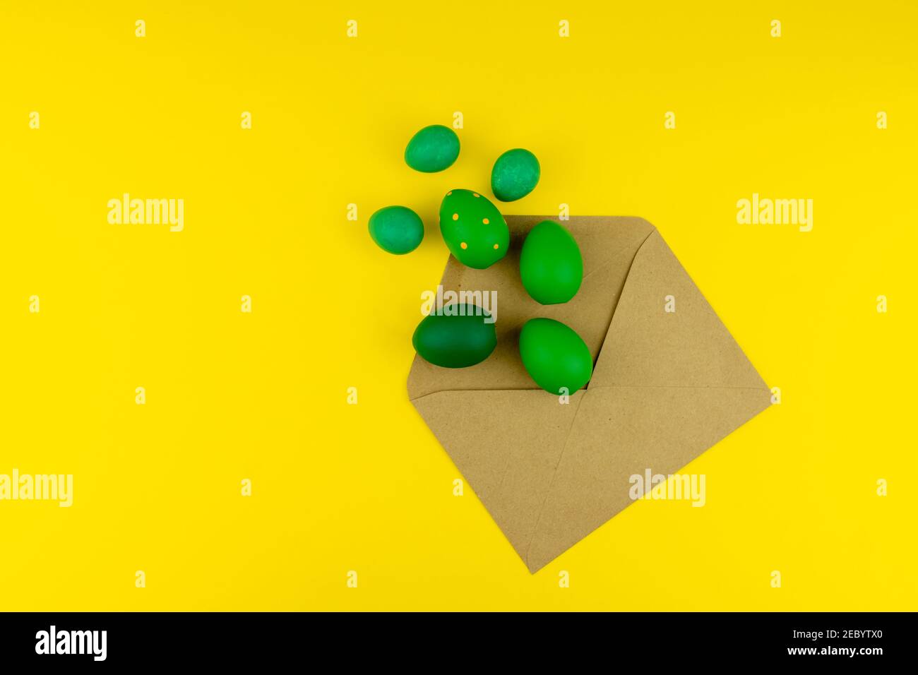 Spring Easter layout with green feathers and eggs, craft envelope on yellow background. Copy space for text for text Stock Photo