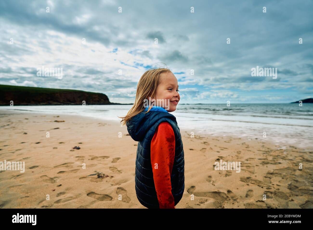 A little preschooler boy is standing on the beach on a winter day Stock Photo