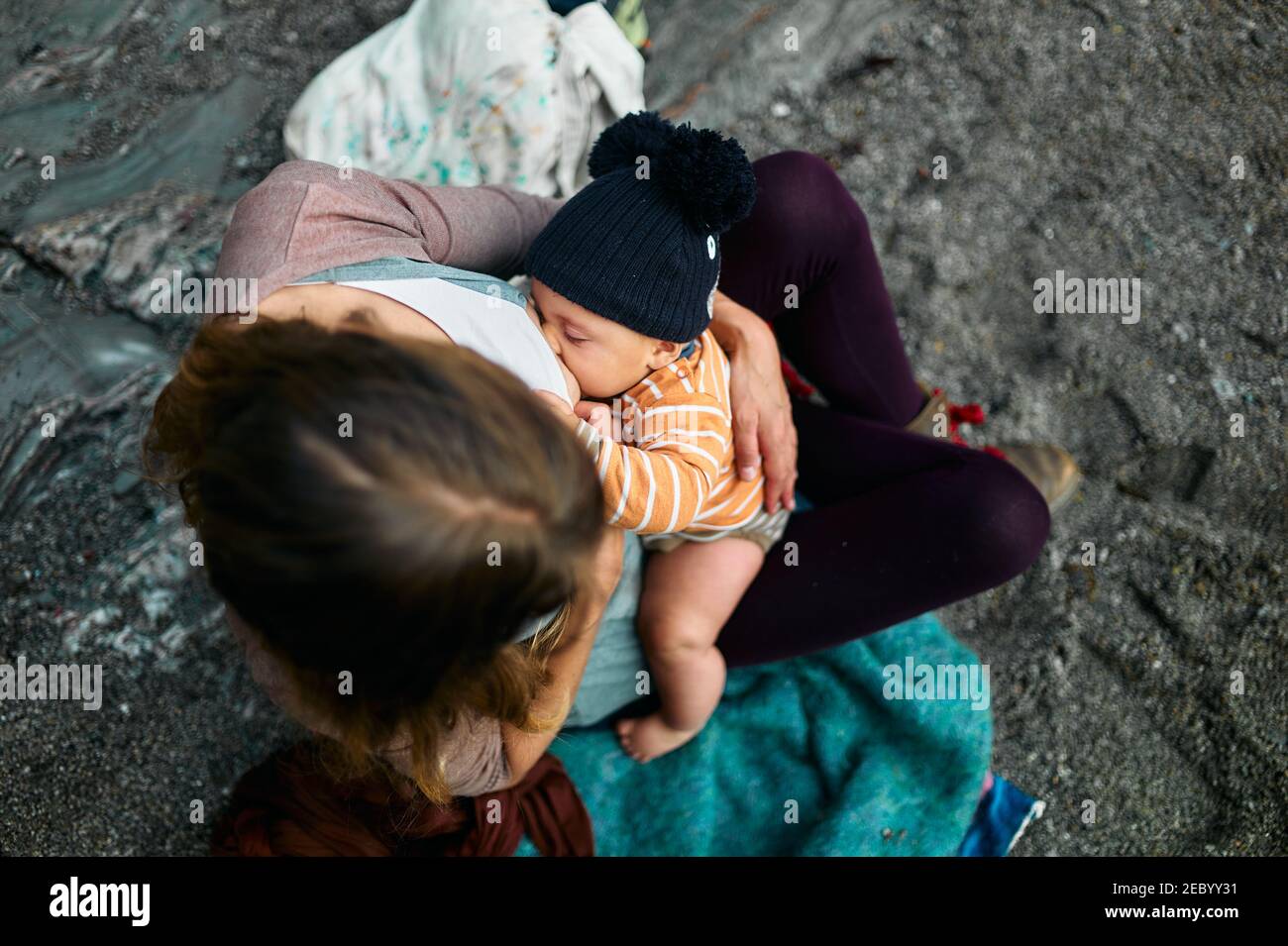 A young mother is breastfeeding her baby outdoors on the beach in autumn Stock Photo