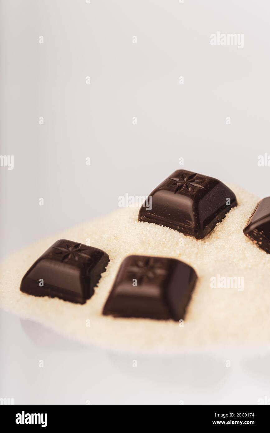 Dark chocolate squares on a pile of raw sugar cane is isolated on a white background Stock Photo