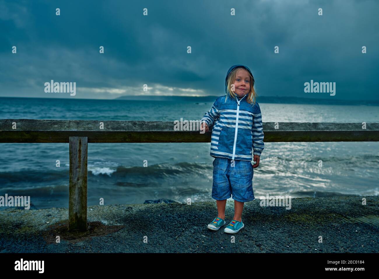 A little preschooler is standing by the sea on a stormy day Stock Photo