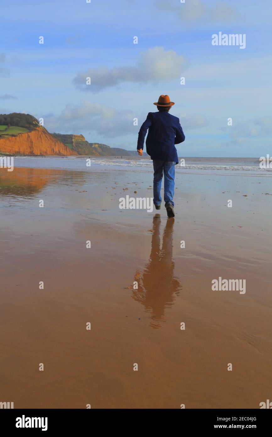 Man with hat running on the sandy beach Stock Photo