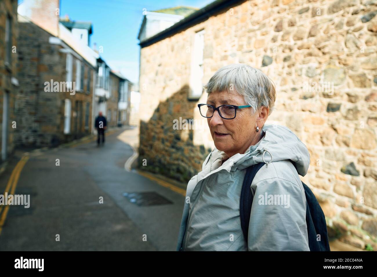A senior woman is standing in the strreet in an english village with stone walls Stock Photo