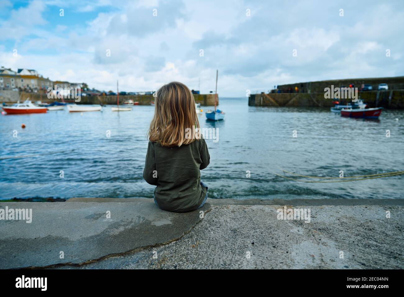A little preschooler is sitting in the harbour of an english fishing village Stock Photo