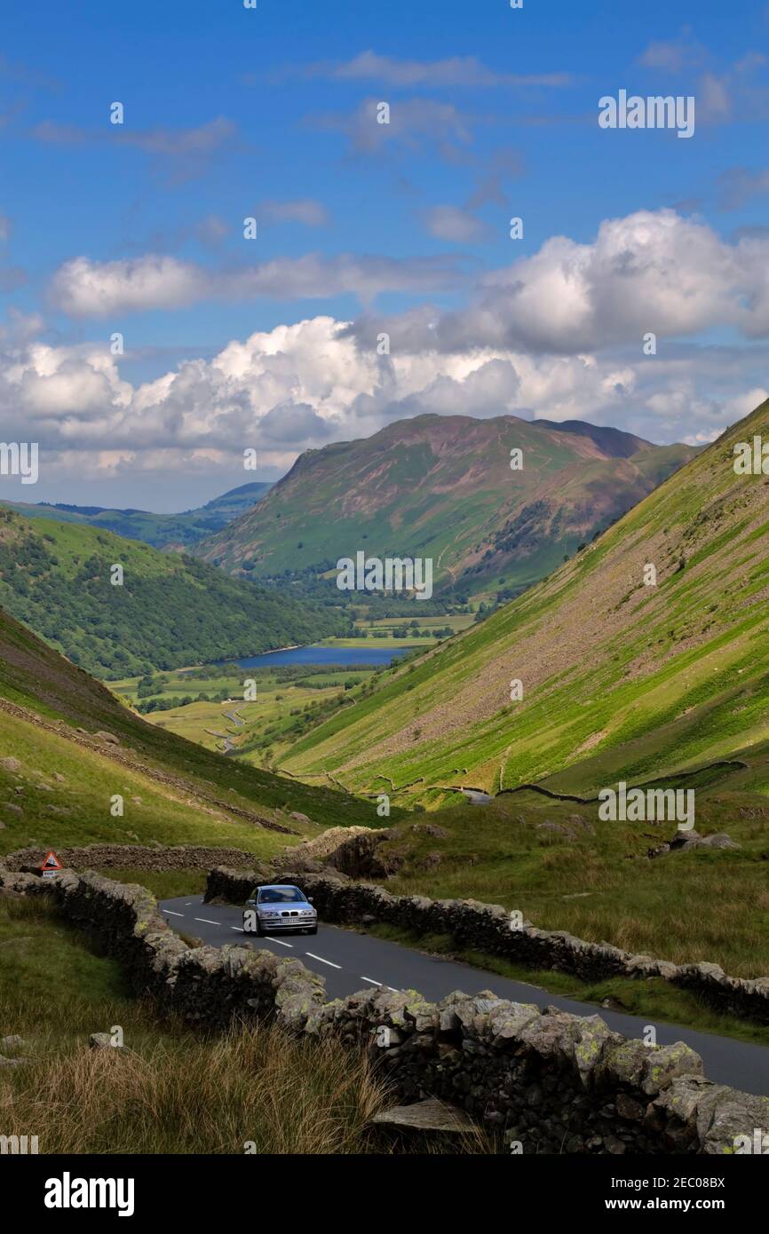 Car climbing Kirkstone Pass with Brothers Water and Patterdale in the distance. Kirkstone Pass is the Lake District's highest pass. Stock Photo