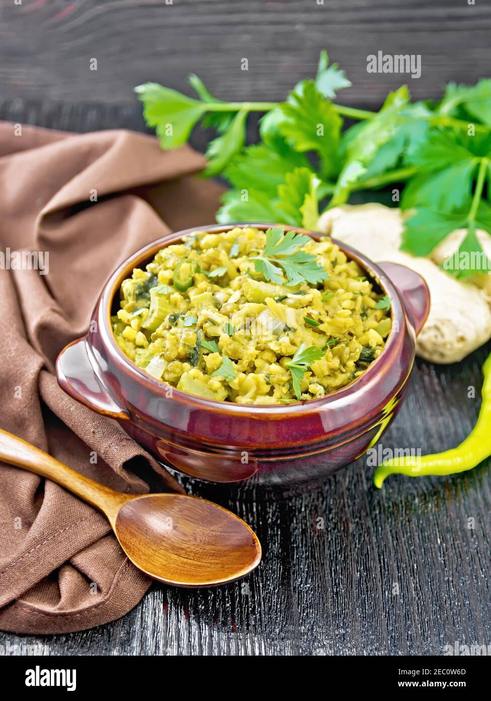 Indian national dish of kichari of mung bean, rice, celery, spinach, hot pepper and spices in a bowl on a napkin, ginger and spoon on wooden board bac Stock Photo