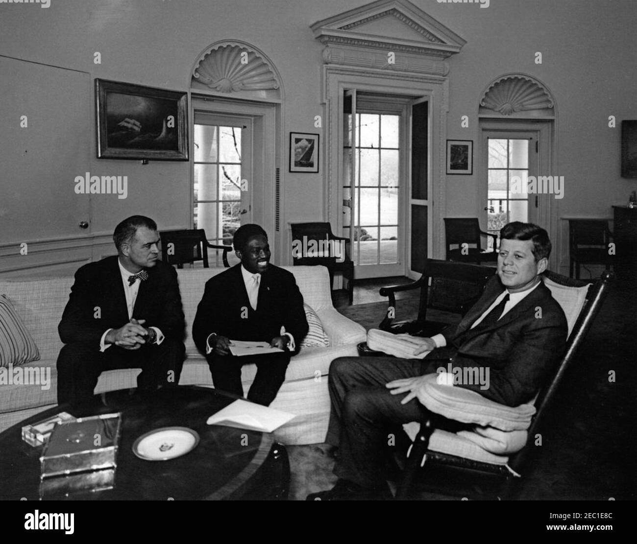 Meeting with Ambassador of Upper Volta, Boureima John Kabore, 12:00PM. President John F. Kennedy (in rocking chair) meets with newly-appointed Ambassador of the Republic of Upper Volta, John Boureima Kaboru00e9; Ambassador Kaboru00e9 presented his credentials to President Kennedy. Assistant Secretary of State for African Affairs, G. Mennen u0022Soapyu0022 Williams, sits at left. Oval Office, White House, Washington, D.C. Stock Photo