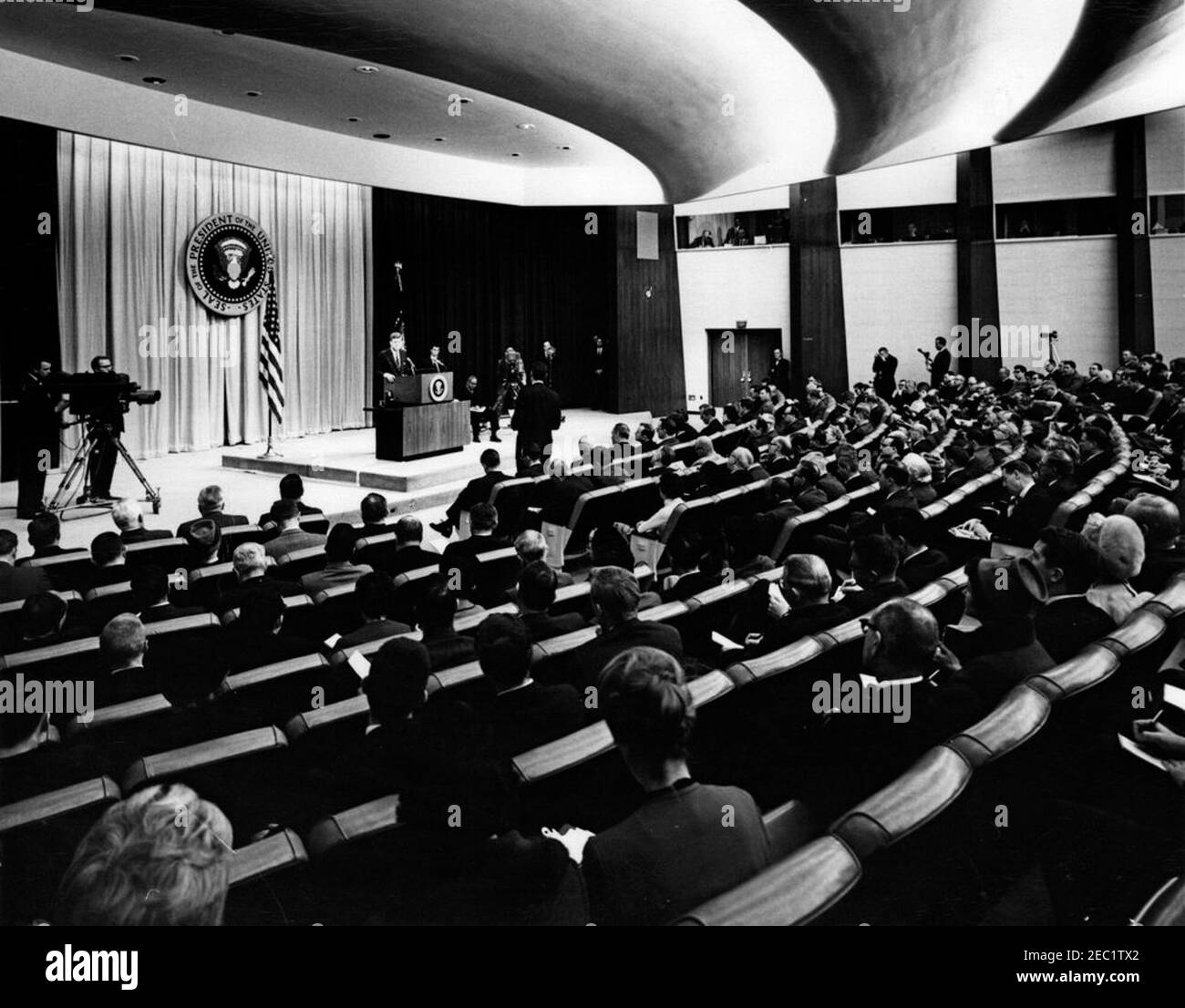 Press Conference, State Department Auditorium, 4:00PM. President John F. Kennedy (at lectern) speaks to reporters during a press conference in the State Department Auditorium, Washington, D.C. Associate Press Secretary Andrew Hatcher sits onstage, right of the lectern. Stock Photo