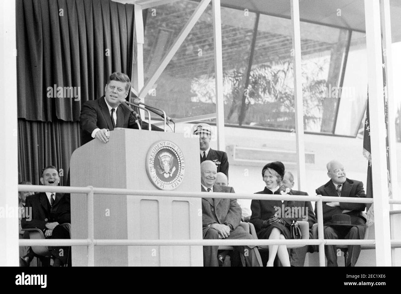 Dedication ceremonies, Dulles International Airport, 11:12AM. President John F. Kennedy (at lectern) delivers remarks at the dedication ceremony for Dulles International Airport, named after the late Secretary of State, John Foster Dulles. Also pictured on speakersu2019 platform: Representative Oren Harris of Arkansas (behind lectern); former president, General Dwight D. Eisenhower; Naval Aide to the President, Captain Tazewell T. Shepard, Jr. (standing); Aline B. Saarinen (widow of the architect for the airport, Eero Saarinen); former director of the Central Intelligence Agency (CIA), Allen Stock Photo